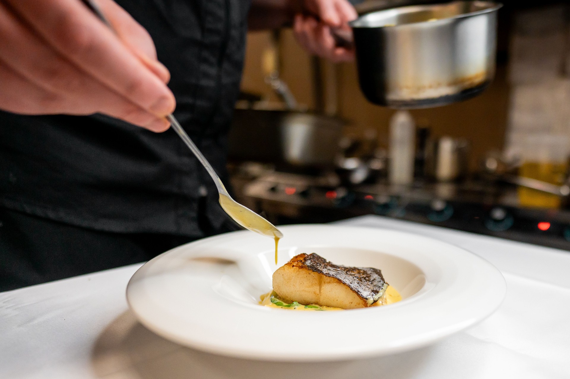 A chef skillfully plating a perfectly cooked piece of fish, drizzled with sauce, showcasing culinary artistry in a modern kitchen setting. Focus on fine dining presentation.